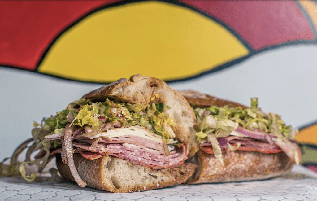 Italian sandwich closeup with deli meats, cheese, and lettuce on deli paper for wrapping. 